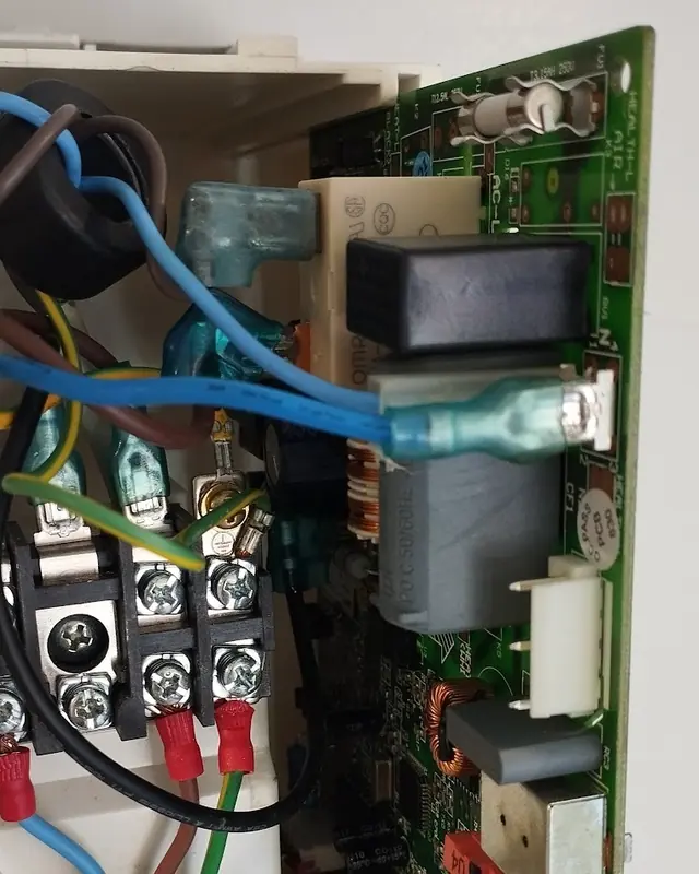 Placa eletrônica verde instalada dentro da unidade de um ar-condicionado, com fusível, relé e régua de bornes